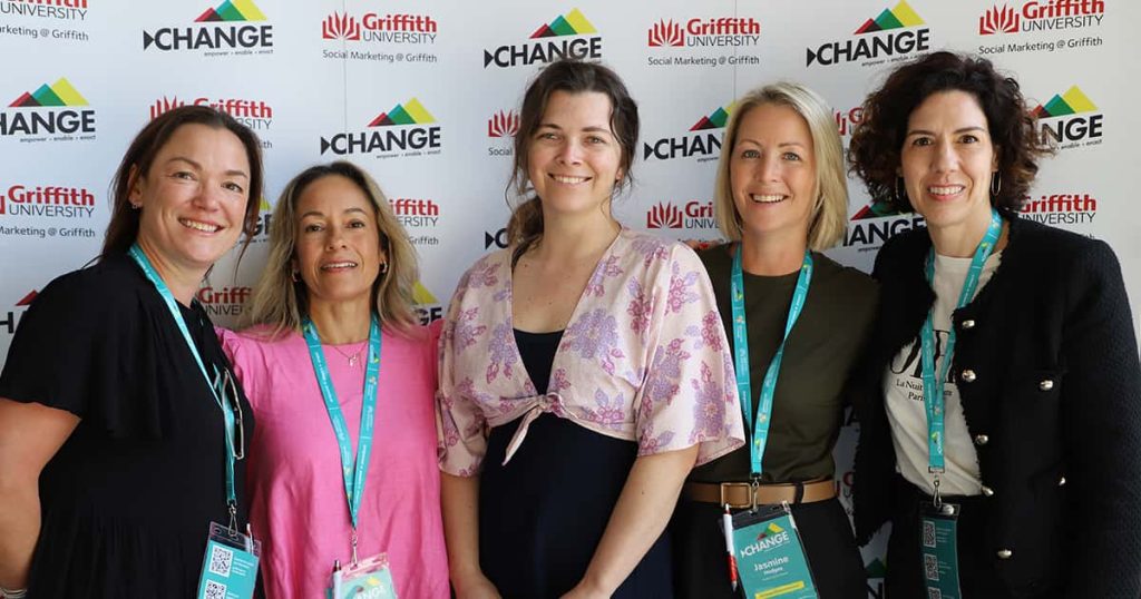 Five women posing together for a photo in front of the Change Conference media wall