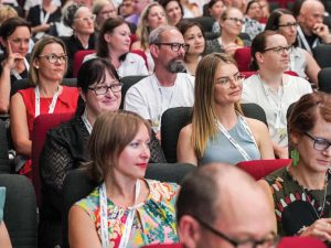A full audience at Change Conference looking towards the front expect for one woman looking at the camera and smiling.