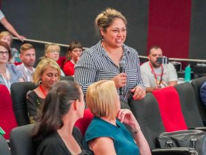 An audience member at Change Conference standing with microphone looking at speakers to ask a question