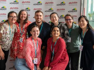 Change conference attendees posing together for photo in front of the media wall