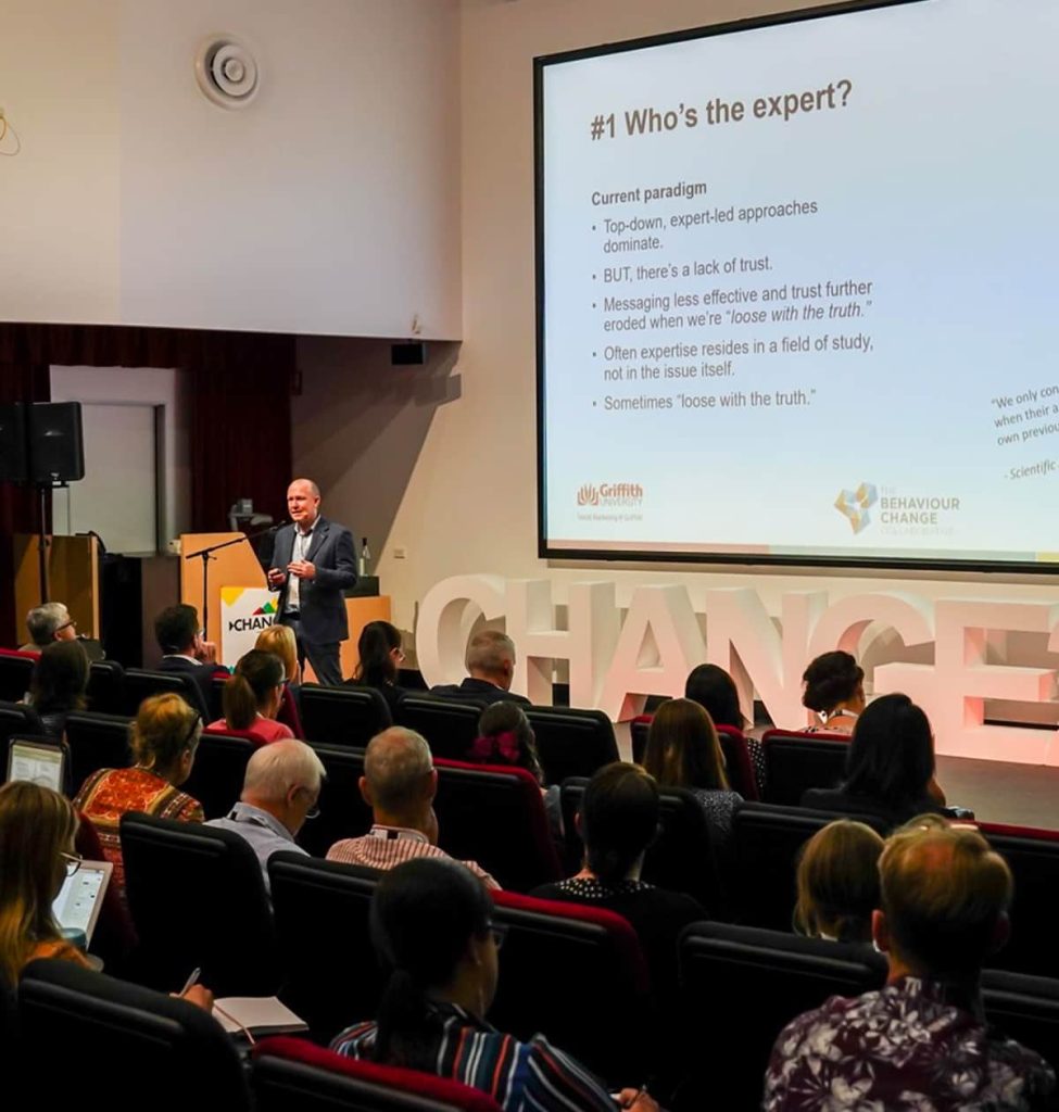 Male speaker at Change Conference standing in front of his presentation looking at the audience