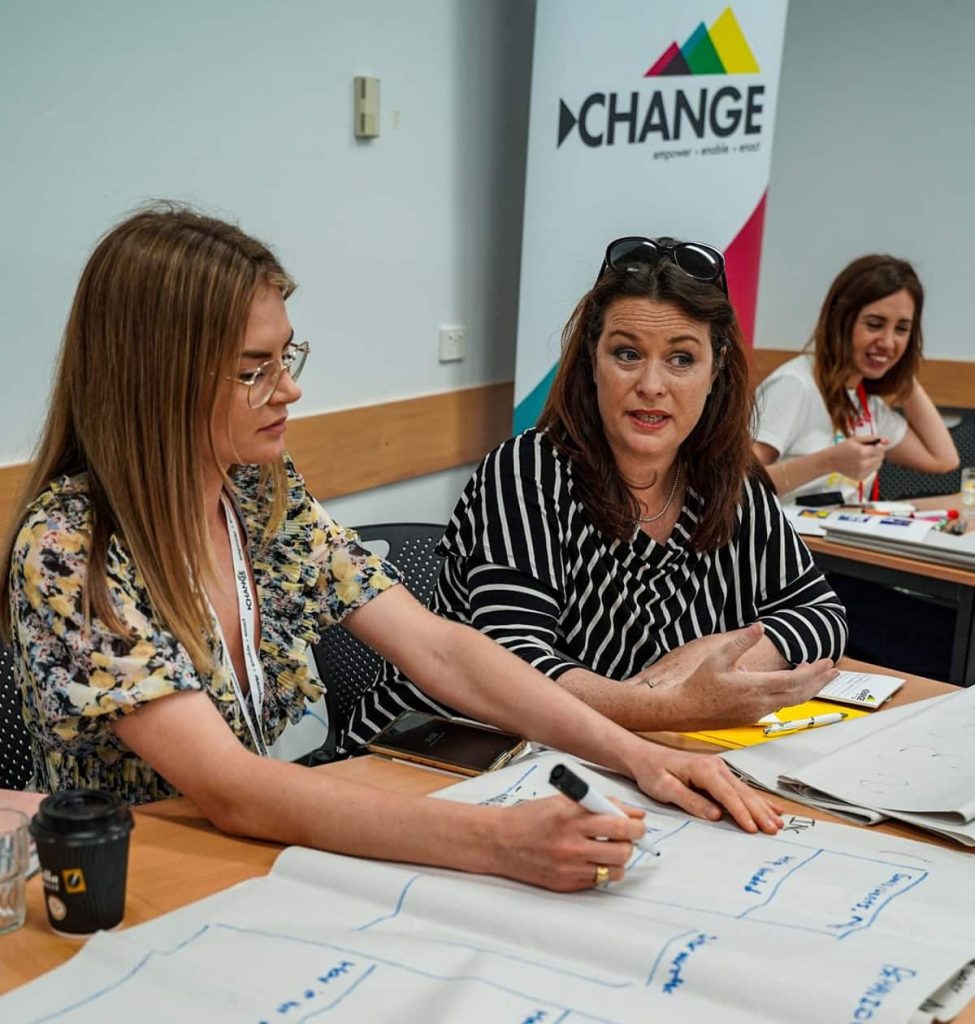 Two women sitting at a table at a Change Conference workshop discussing their projects.