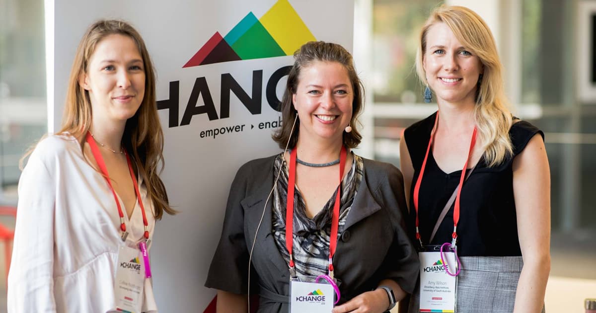 Three women standing together in front of a Change Conference banner smiling at the camera